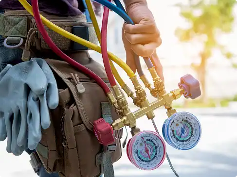 Person holding HVAC manifold gauge set and wearing a tool belt with gloves attached, outdoors in daylight.