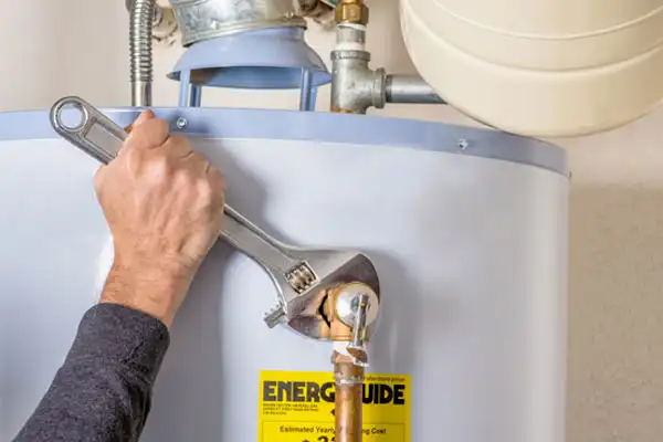 A friendly Childers technician uses an adjustable wrench to tighten a valve on a water heater during a professional service visit.