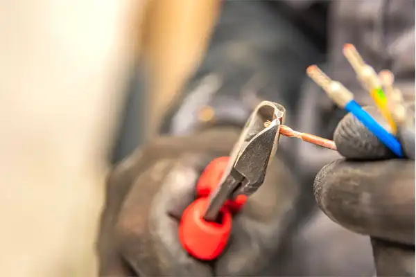 A Childers technician wearing gloves uses wire cutters to carefully strip the end of a copper electrical wire.